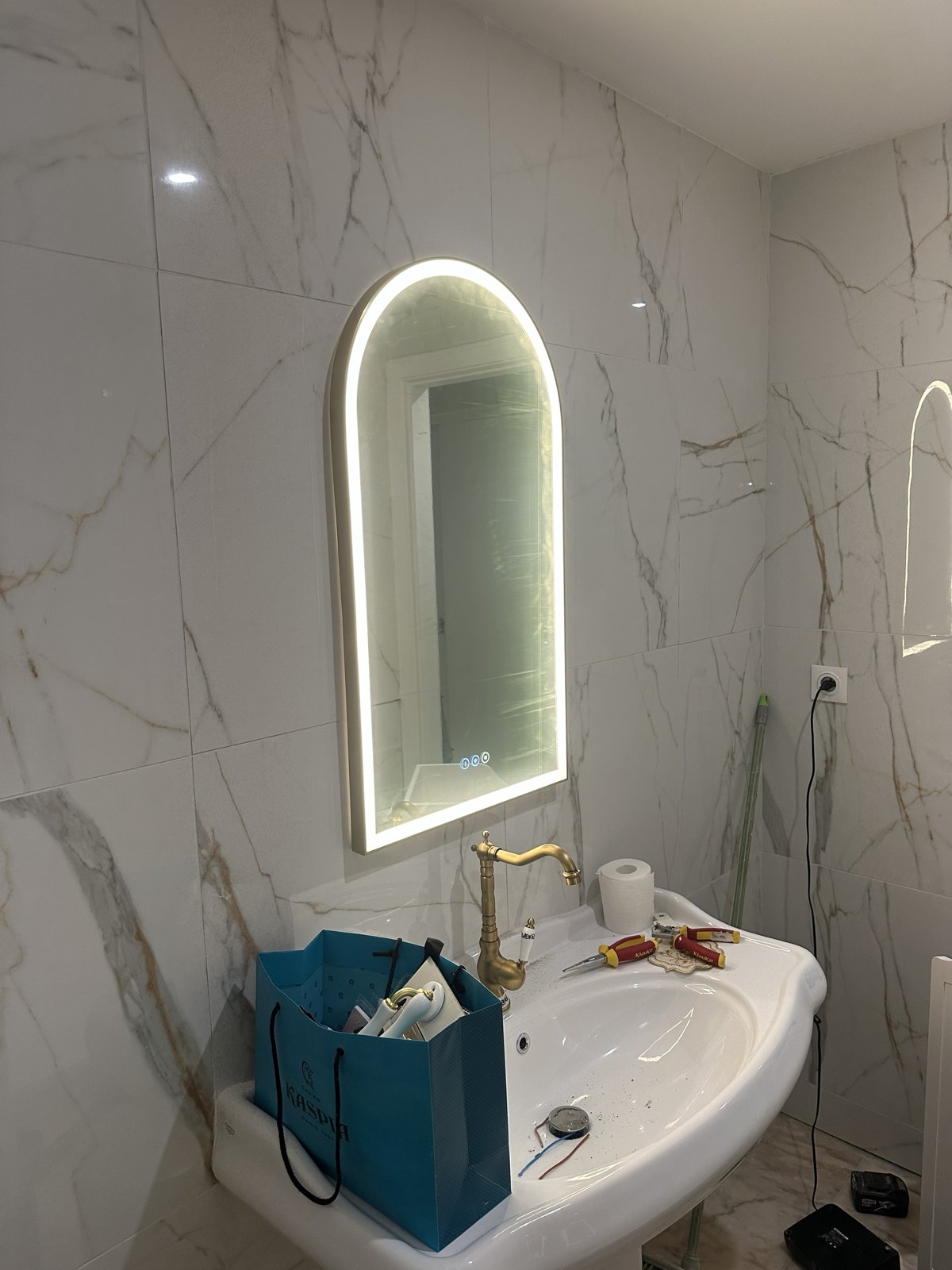 Miroir LED arqué posé et raccordé dans une salle de bain en marbre